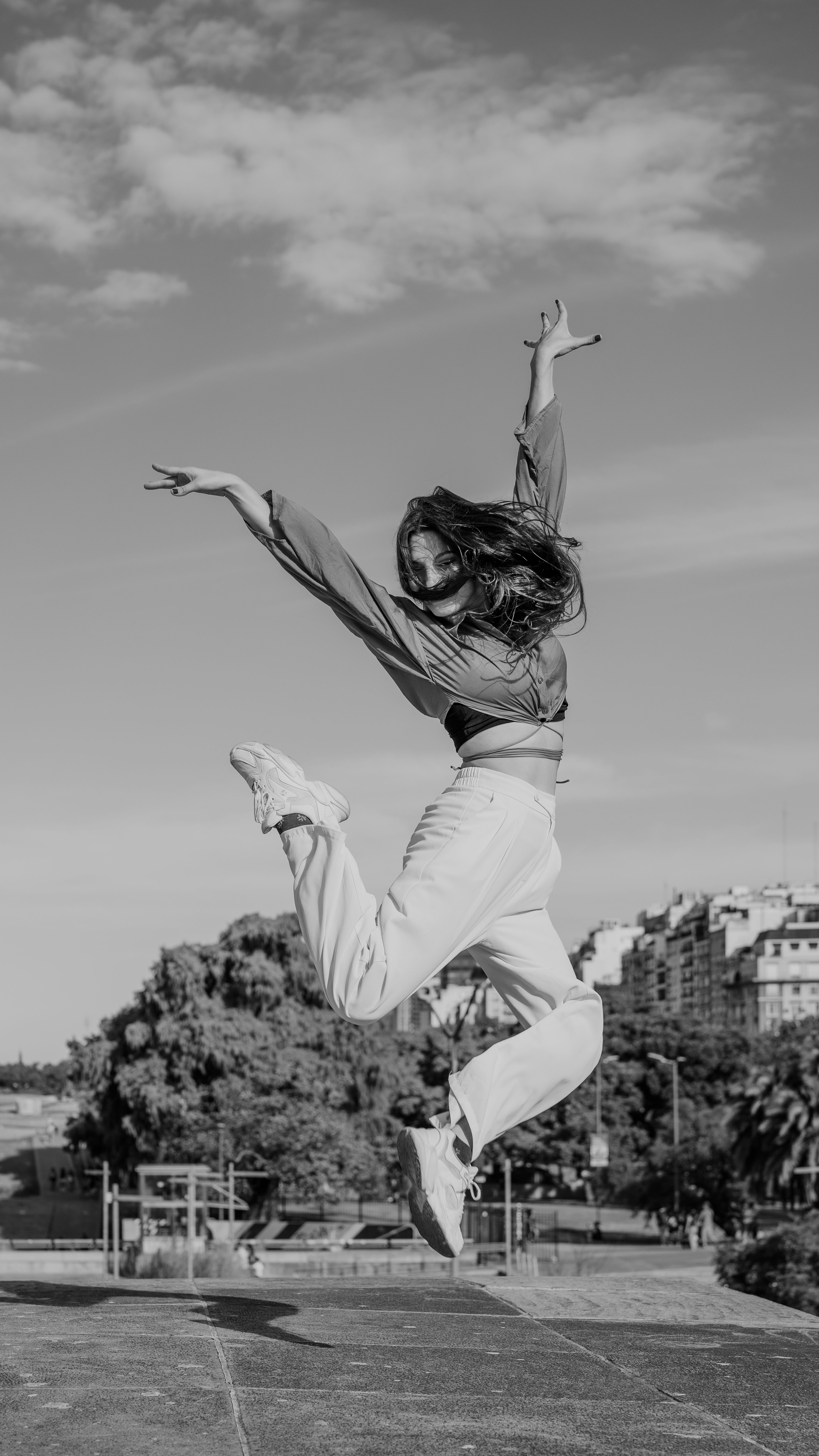 A young woman in mid-air doing a dance leap in an urban setting, captured in black and white.