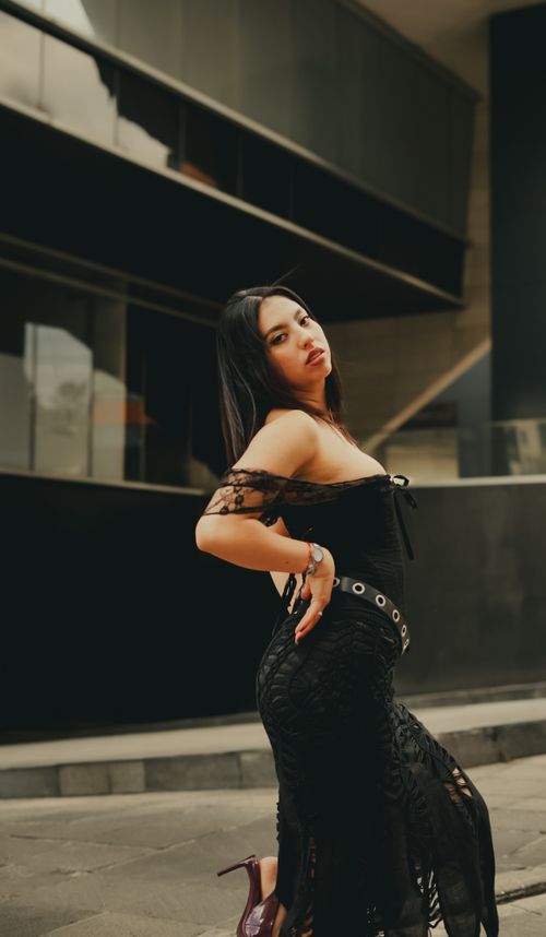 Free Confident woman in black dress striking a pose in an urban setting, showcasing modern fashion. Stock Photo