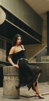 Stylish woman in black lace dress posing confidently in a modern urban environment.