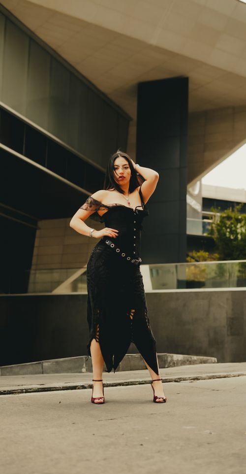 Free A stylish fashion model striking a pose in a modern urban environment, wearing a black dress. Stock Photo