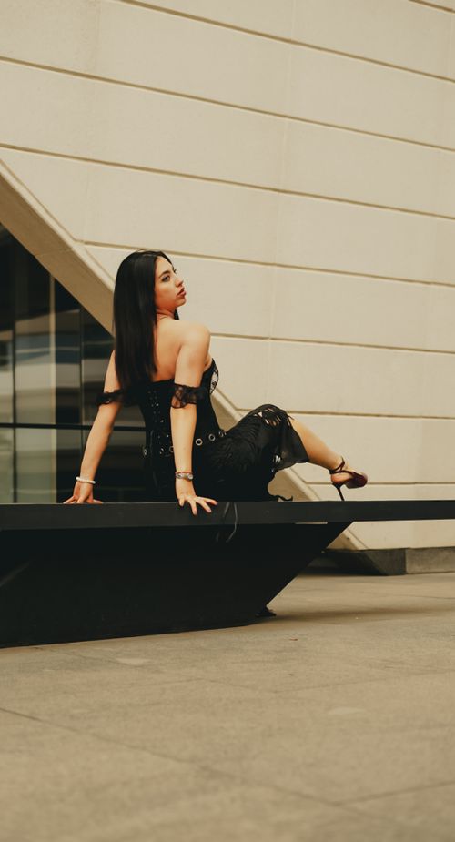 Free Stylish woman in black dress poses confidently on a modern architectural structure outdoors. Stock Photo