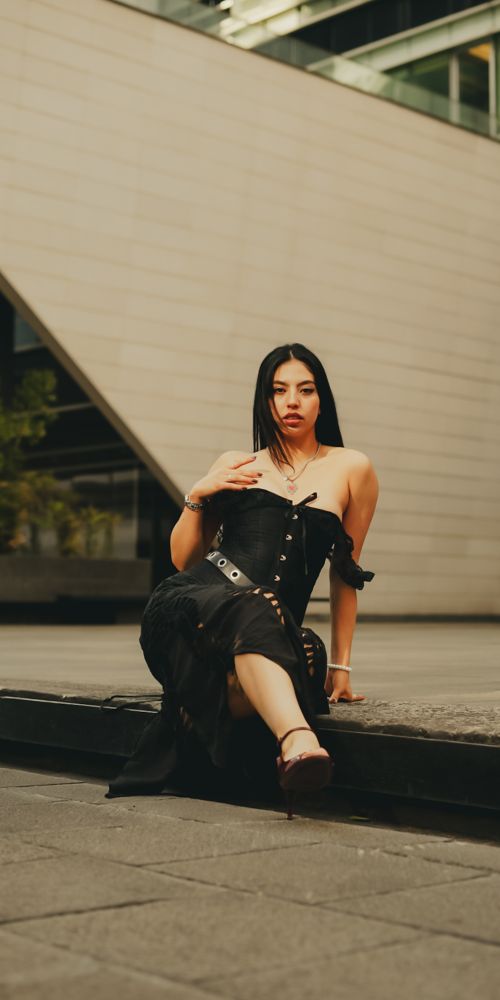 Free Stylish woman in a black dress posing outdoors against modern architecture. Stock Photo