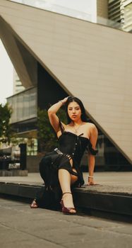 Woman in stylish black attire posing in front of modern architecture in an urban environment.