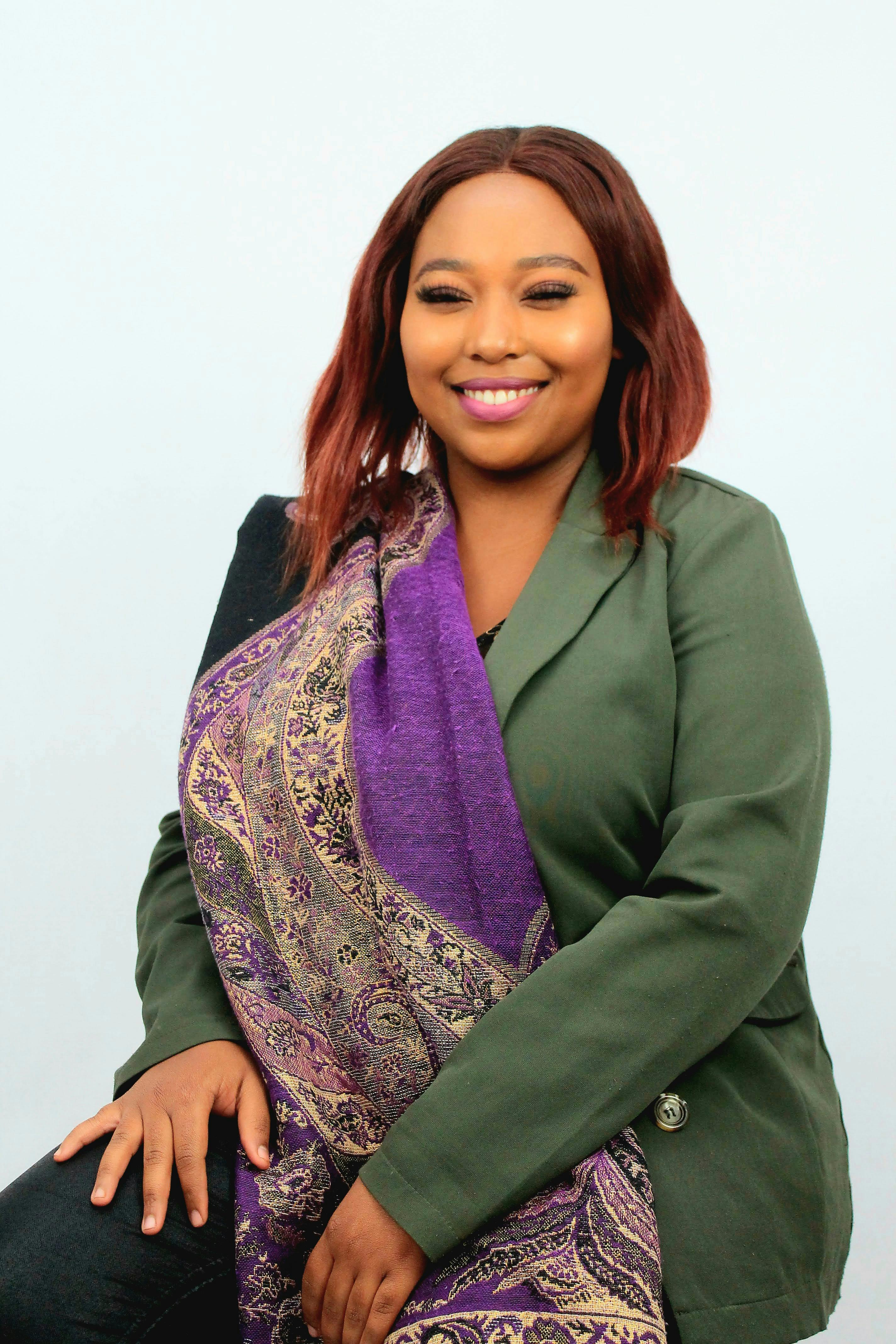 Portrait of a woman wearing a green jacket and purple scarf, smiling confidently.