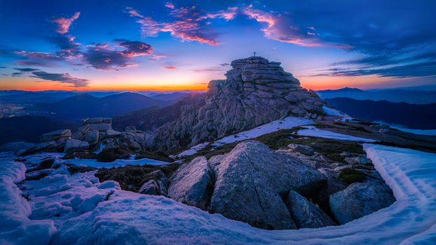 Stunning sunset over a rocky mountain peak with snow patches and vibrant sky hues.