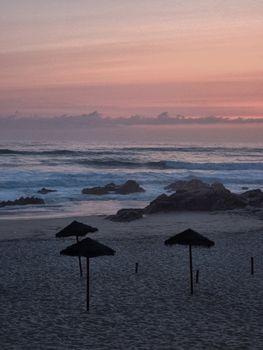 Breathtaking view of a serene beach at sunset with silhouettes of umbrellas and gentle waves.