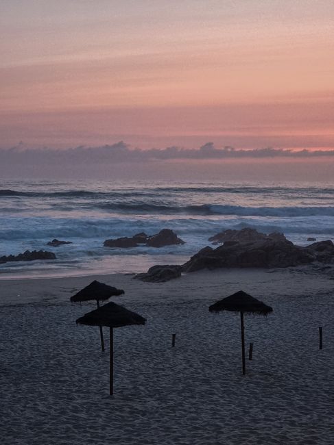 Breathtaking view of a serene beach at sunset with silhouettes of umbrellas and gentle waves.