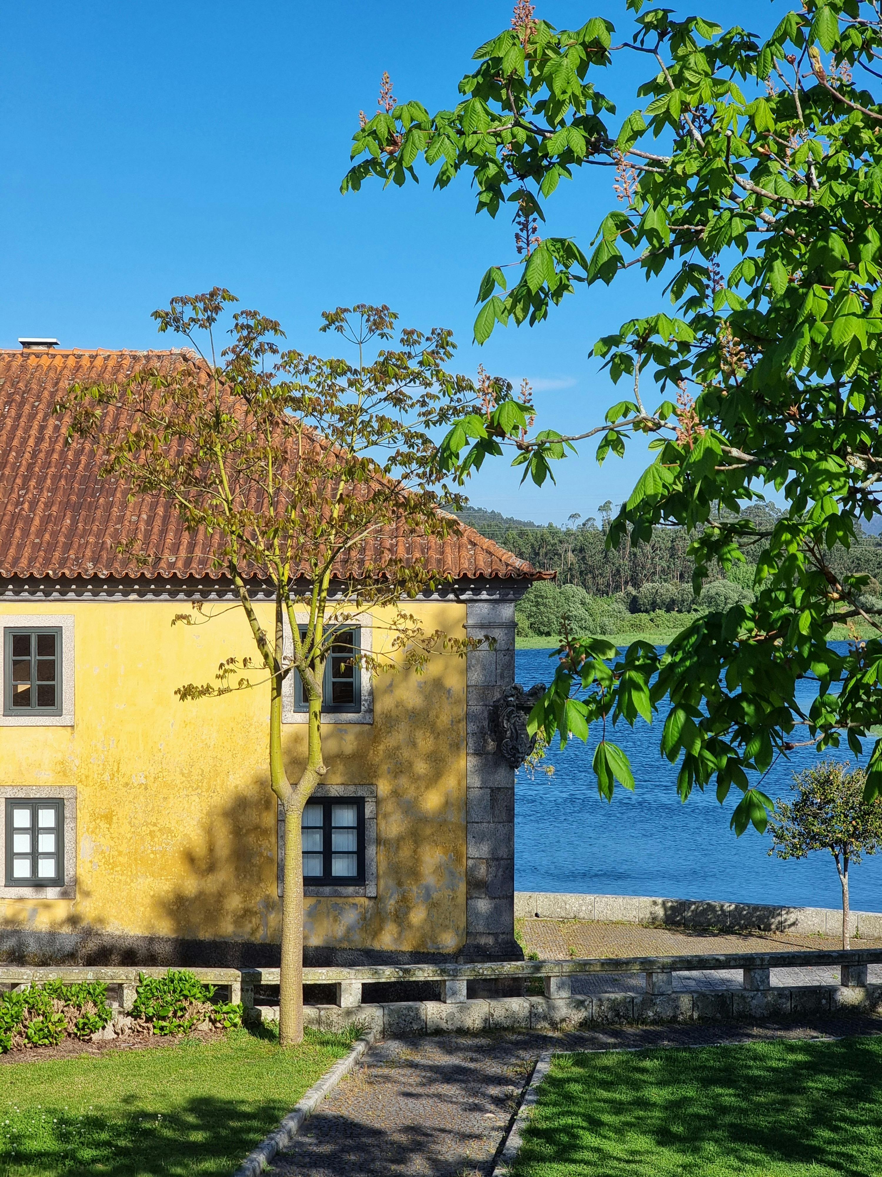 Scenic view of a yellow house by a lake surrounded by lush green trees under a clear blue sky.