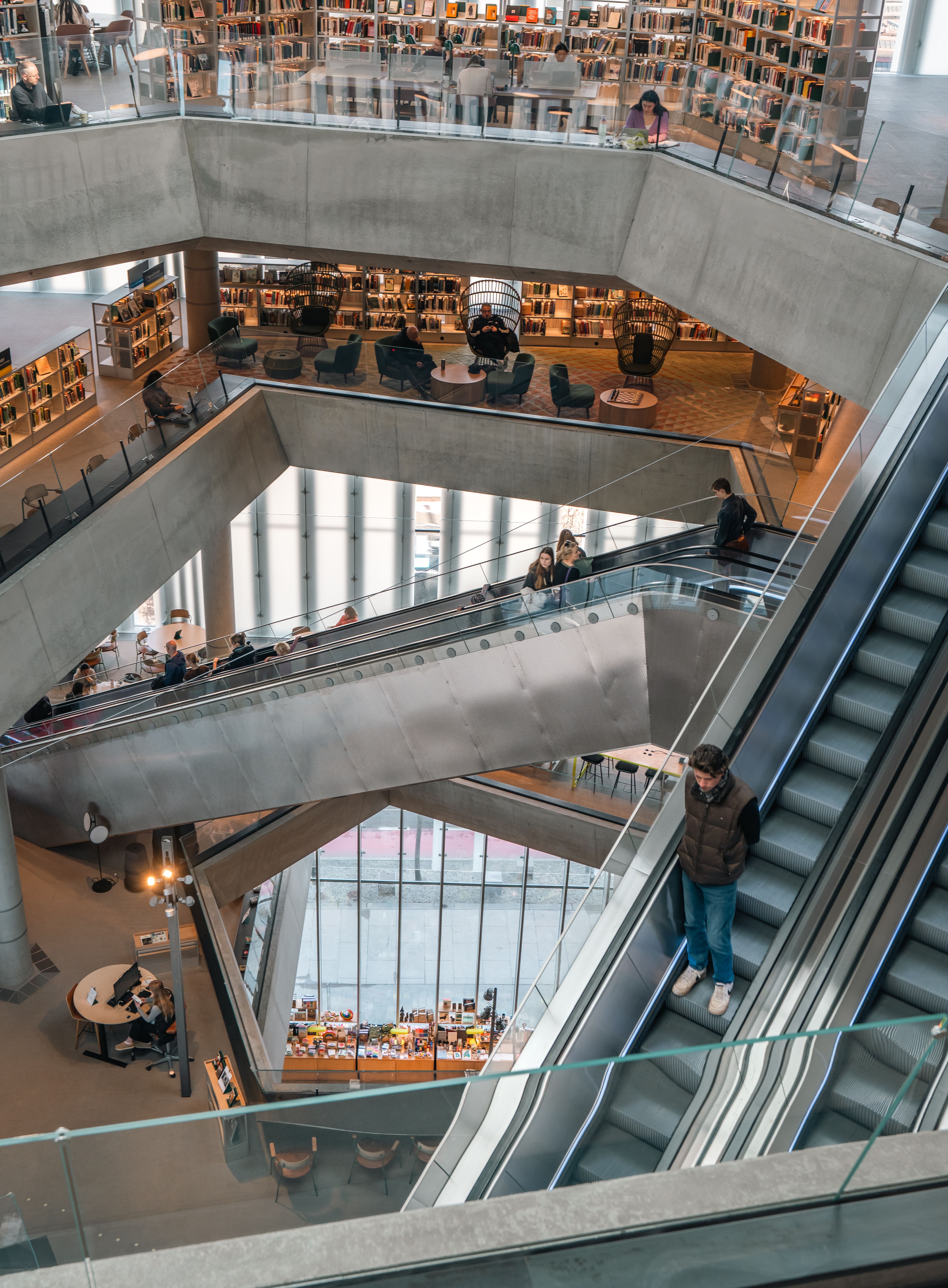 Interior view of a modern multi-level library with escalators and shelves filled with books, bustling with people.