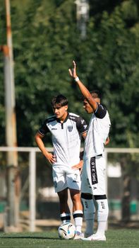Two soccer players in white jerseys plan a strategy on the field outdoors.