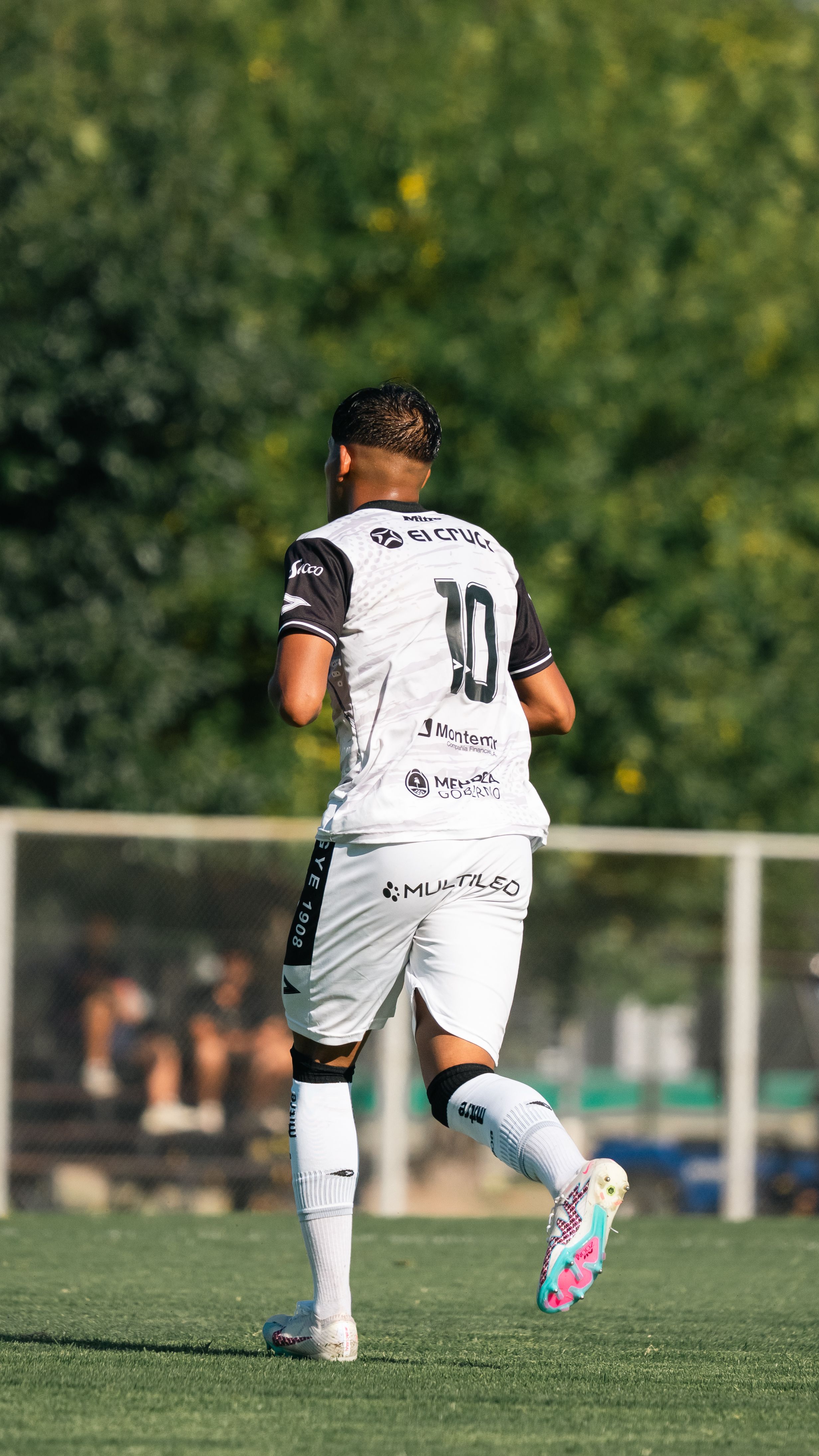 Soccer player in white uniform running on a lush green field.