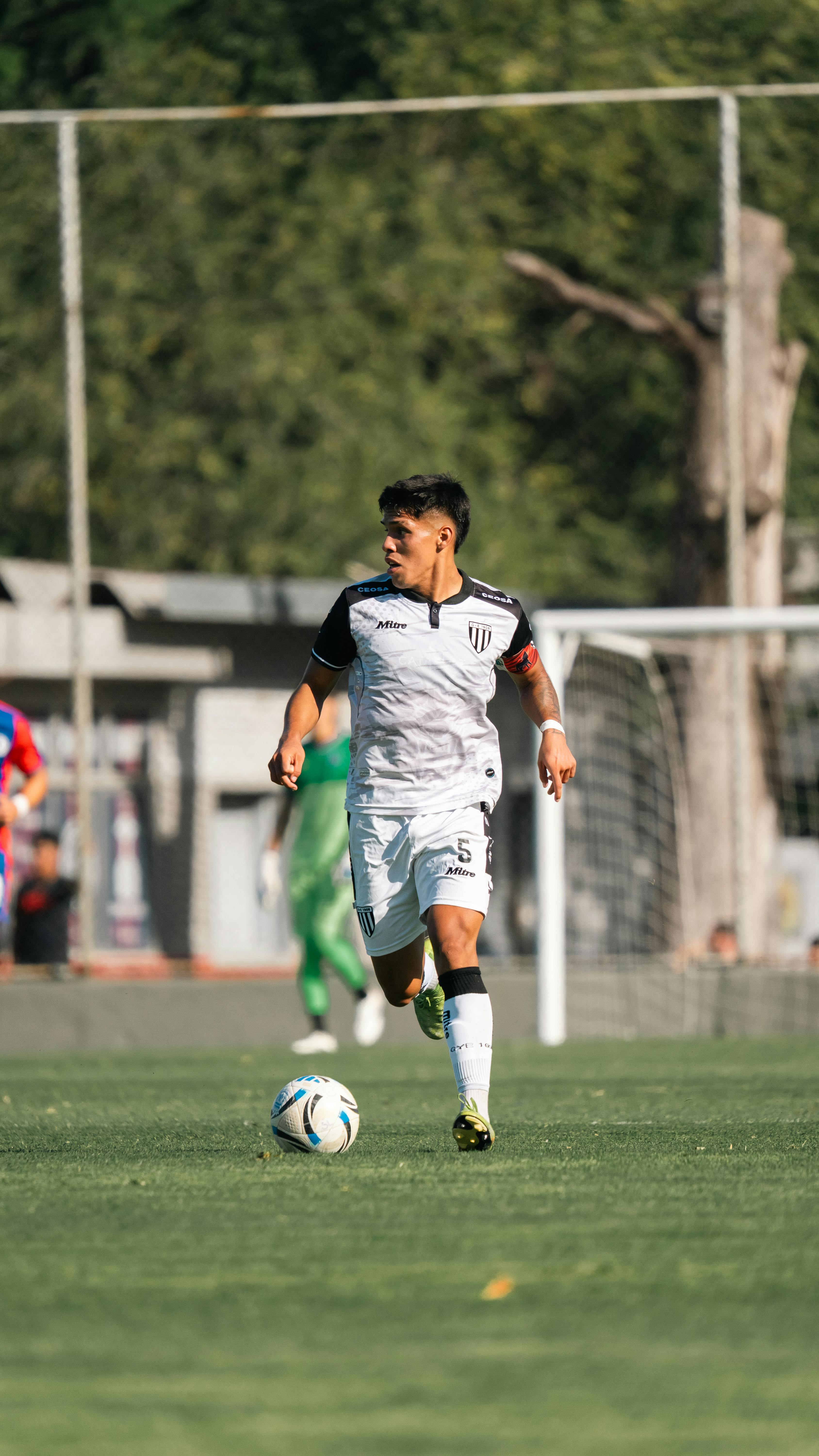 Male soccer player controlling the ball on a sunny outdoor field during a match.
