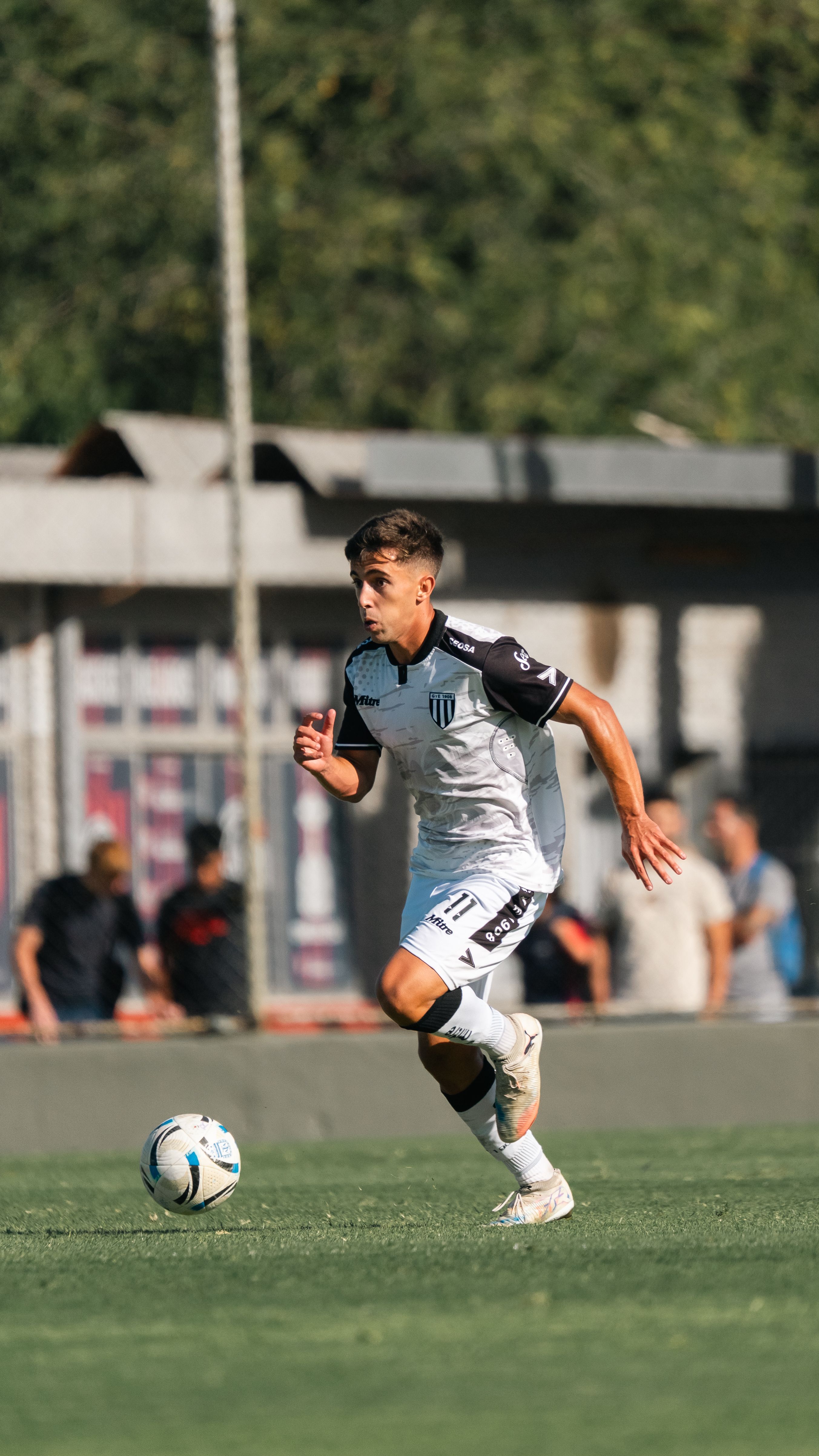 Teen soccer player wearing a black and white uniform dribbling a ball on a grassy field during a daytime match.