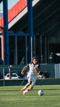 A focused soccer player sprinting on a green field during a game under a stadium.