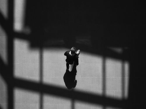 Free A dramatic black and white overhead shot of a person walking, casting shadows on the ground. Stock Photo