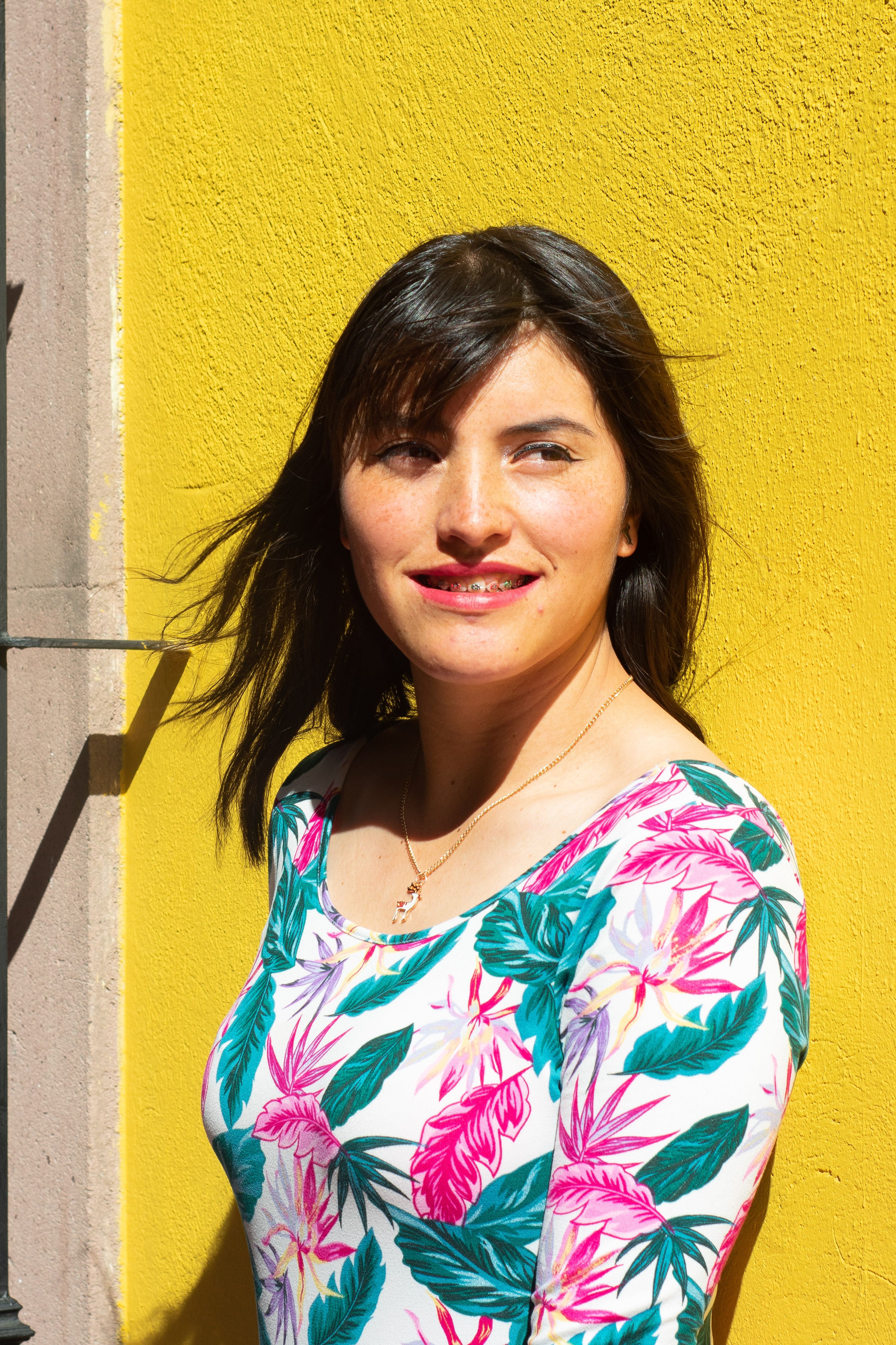 Vibrant portrait of a woman in a floral top against a bright yellow wall in Lerma de Villada, Mexico.