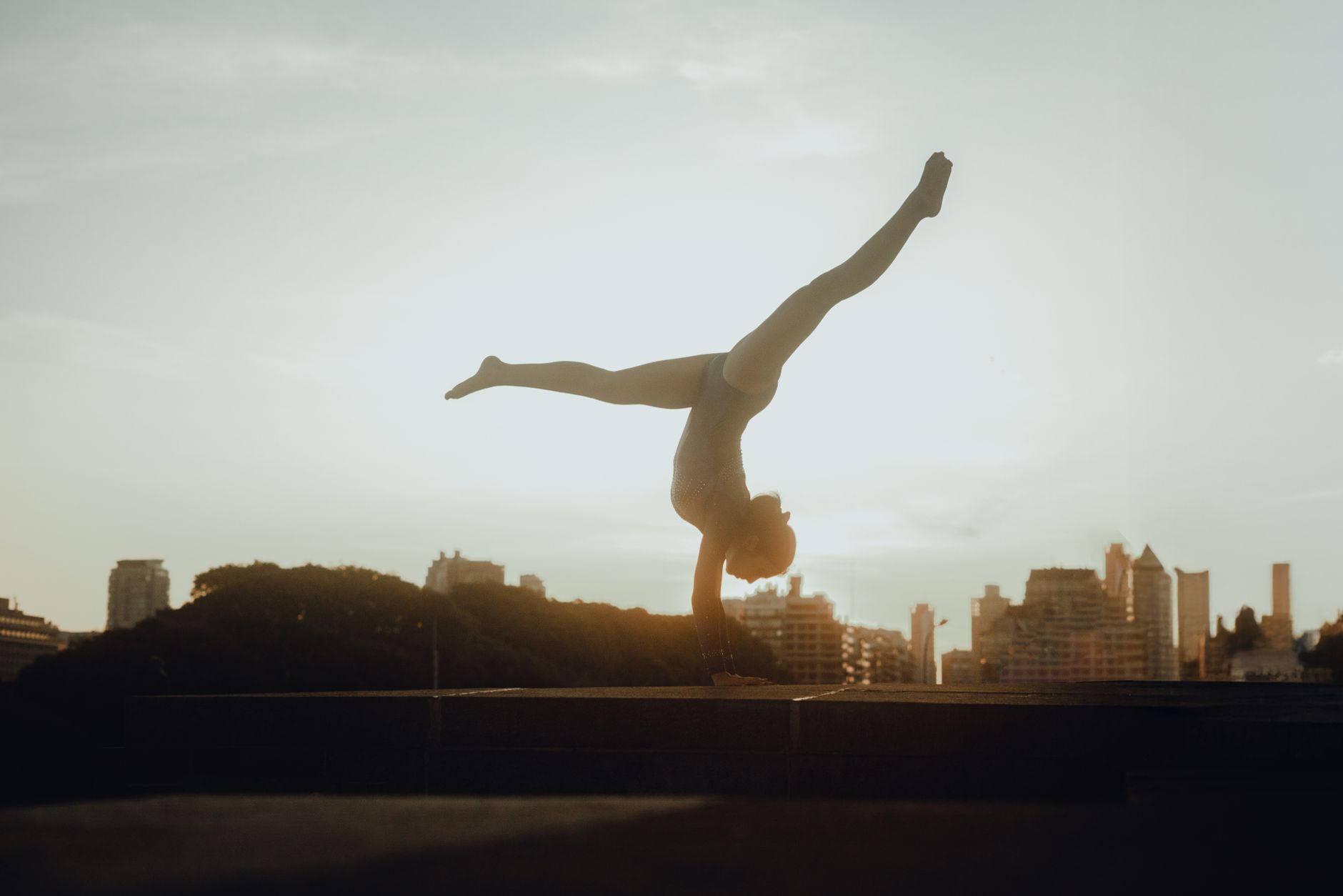 A gymnast performs an impressive handstand against the stunning skyline of Buenos Aires at sunset.
