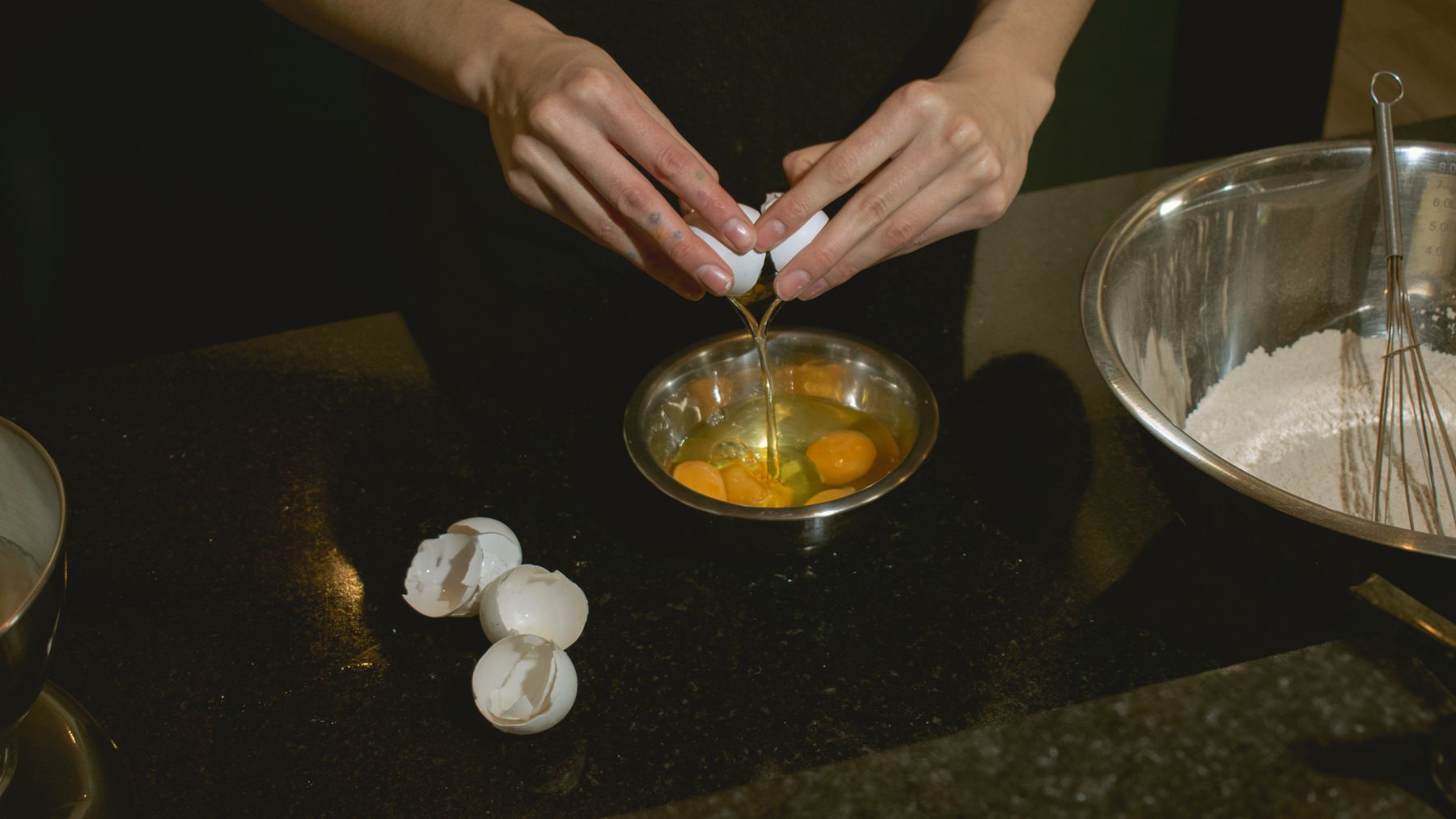 Hands cracking eggs into a bowl, with flour ready for baking. Perfect for culinary scenes.