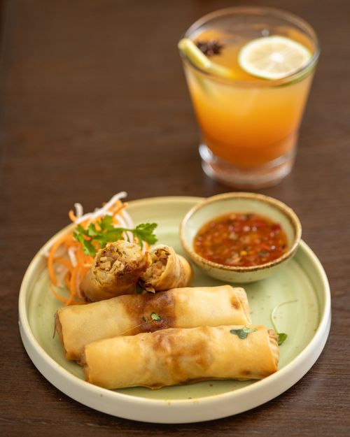 Free Close-up of crispy spring rolls with dipping sauce and a refreshing drink on a table. Stock Photo