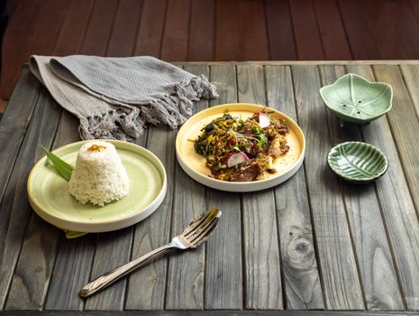 Delicious traditional Indonesian meal with rice and vegetables on a rustic wooden table setting.