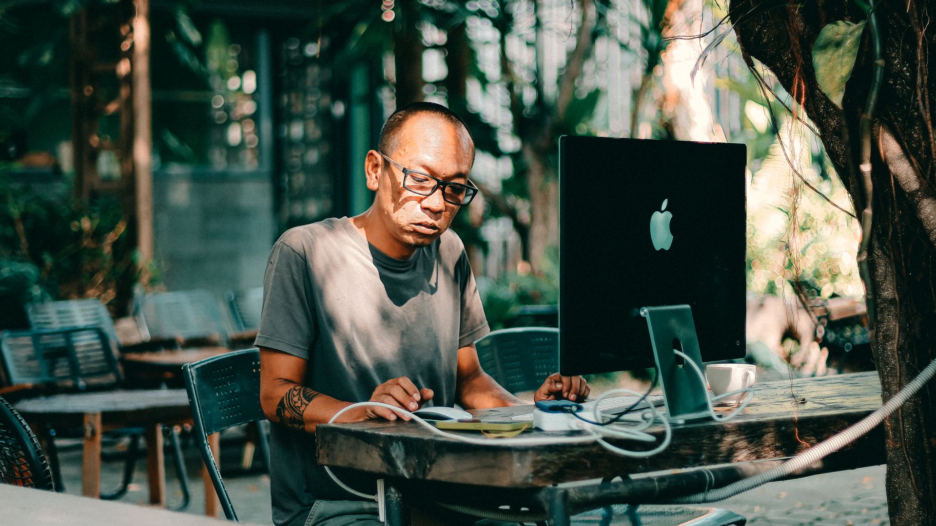 Modafinil for Freelance Writers: Enhancing Productivity Adult man with glasses working on a computer outdoors in a sunny cafe setting — modafinil for freelance writers