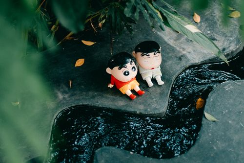 Free Adorable cartoon dolls sitting near a flowing stream surrounded by lush greenery. Stock Photo