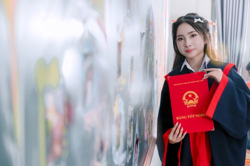 Free A young woman in a graduation gown holding a diploma with a blurred artistic background indoors. Stock Photo