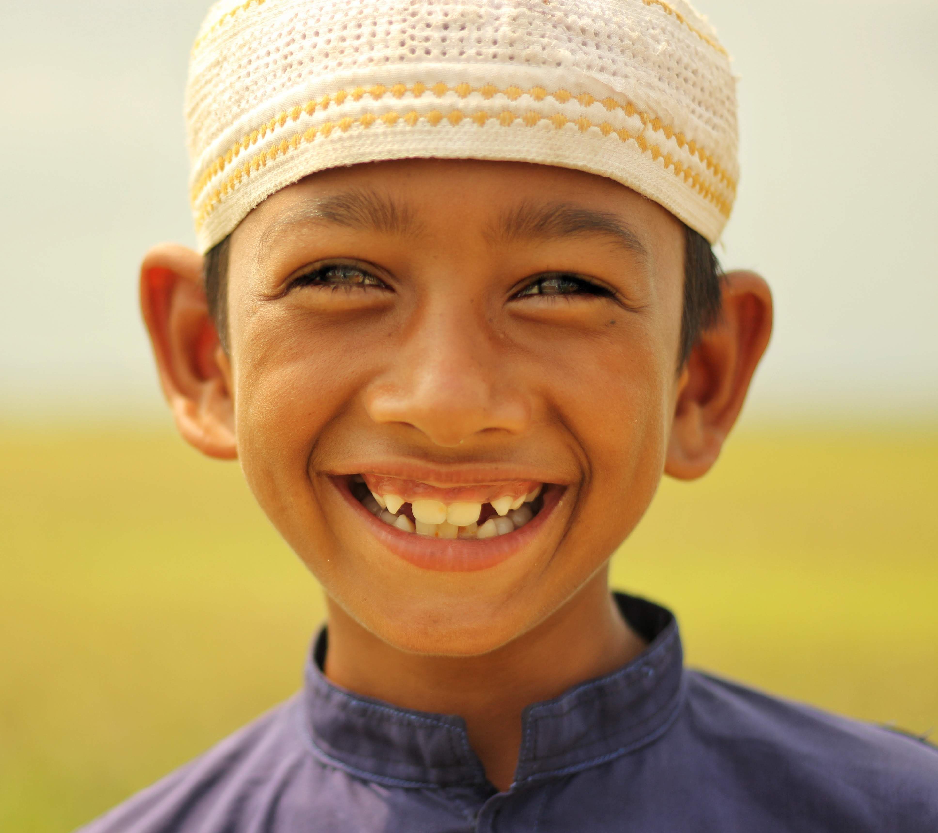 Portrait of a smiling boy wearing a traditional cap, outdoors in Bangladesh.