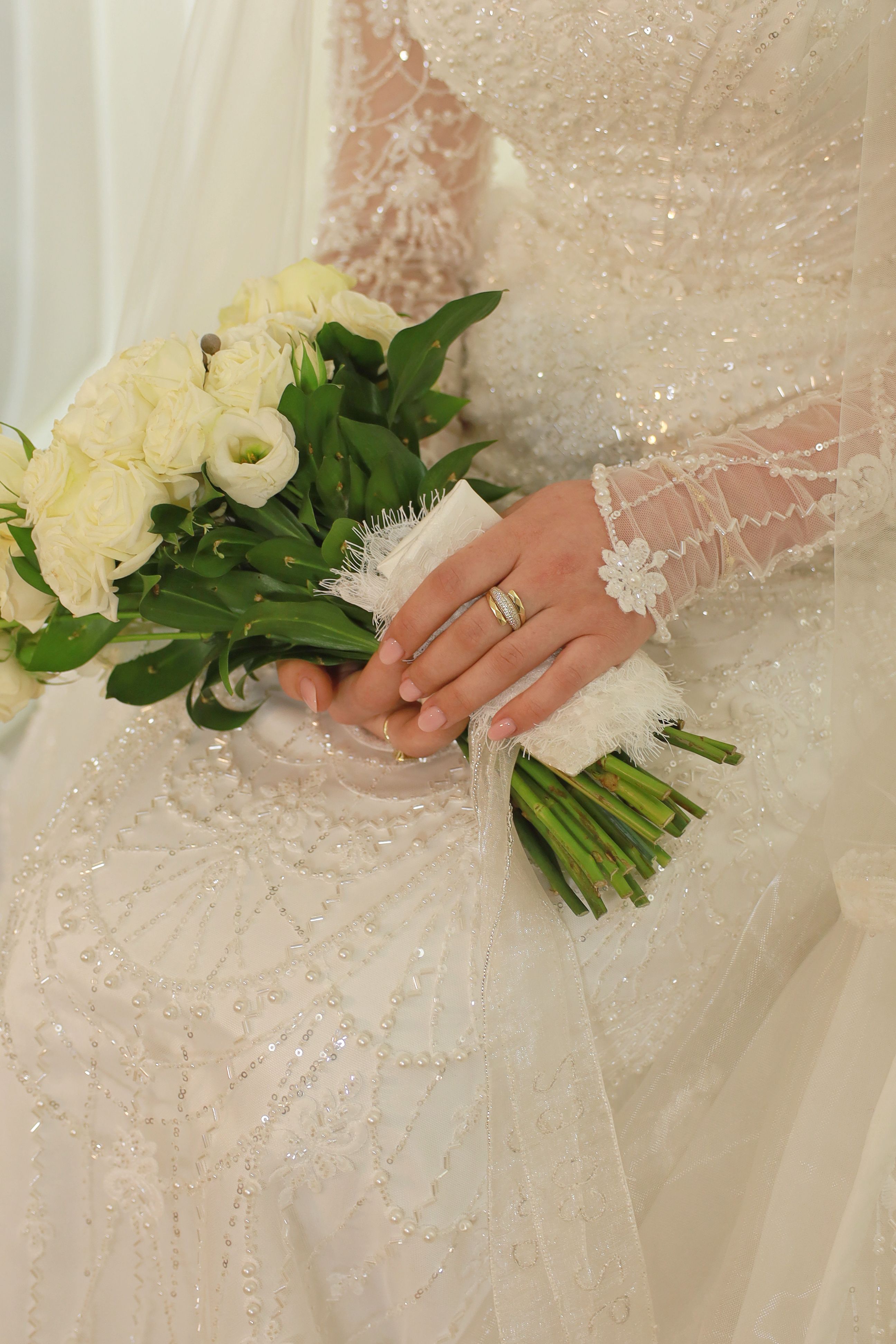 Bride in sparkling gown holds a fresh bouquet of white tulips and roses, showcasing elegance and beauty.