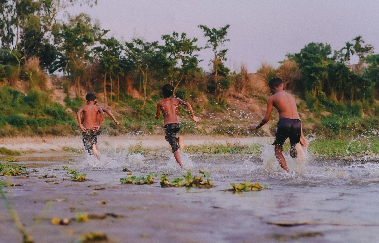 three boys running in a river splashing water during sunset full of jo