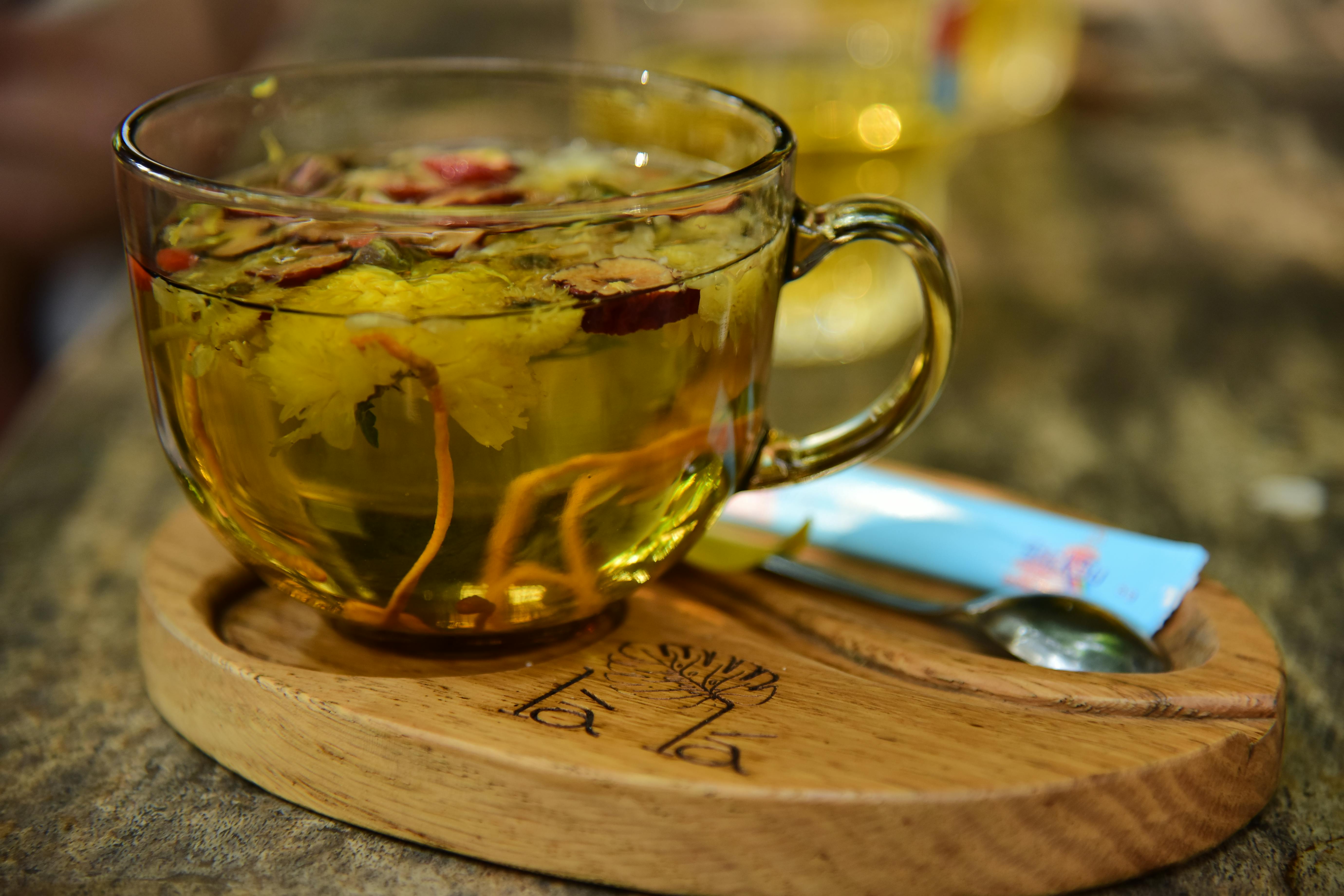 trà kombucha dưỡng nhan - Một tách trà thảo mộc ấm với chanh, được phục vụ kèm táo và hồng trên khay gỗ.