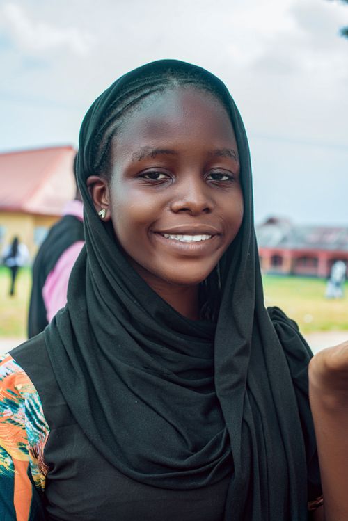 Free A smiling young woman in a black headscarf outdoors with a building in the background. Stock Photo
