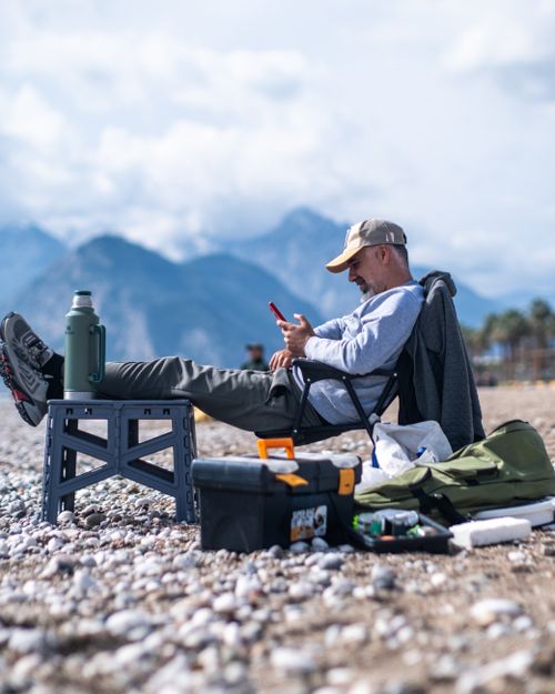 Free Man seated on rocky beach, enjoying leisure time, with mountains in the background. Stock Photo