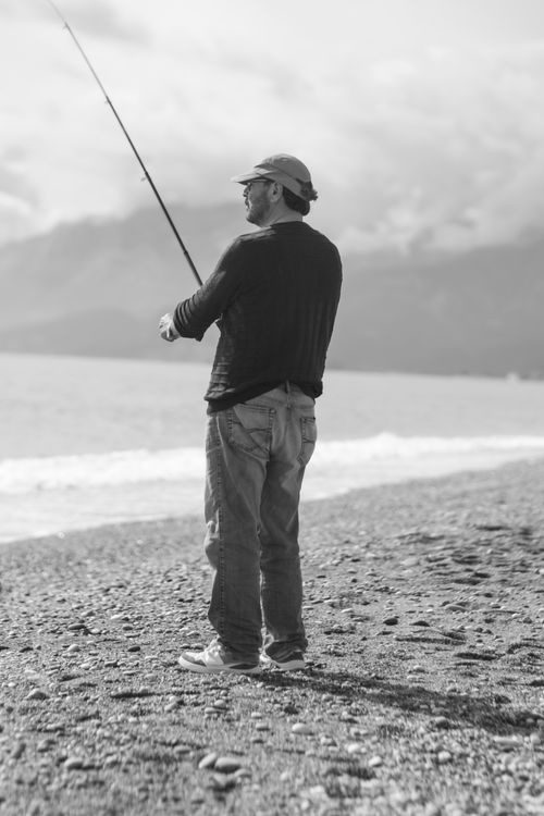 Free A man fishing on a rocky beach under cloudy skies, exuding calmness and focus. Stock Photo