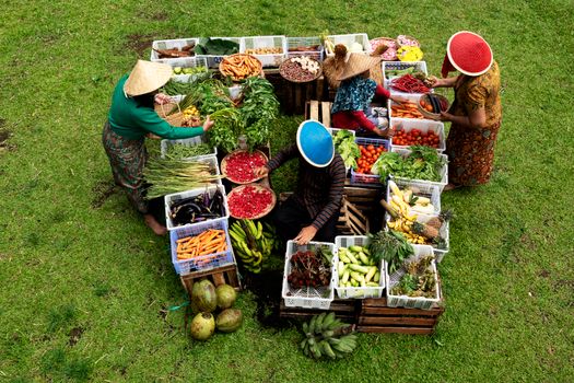 Market vendors arrange fresh produce and vegetables outdoors in a vibrant scene.