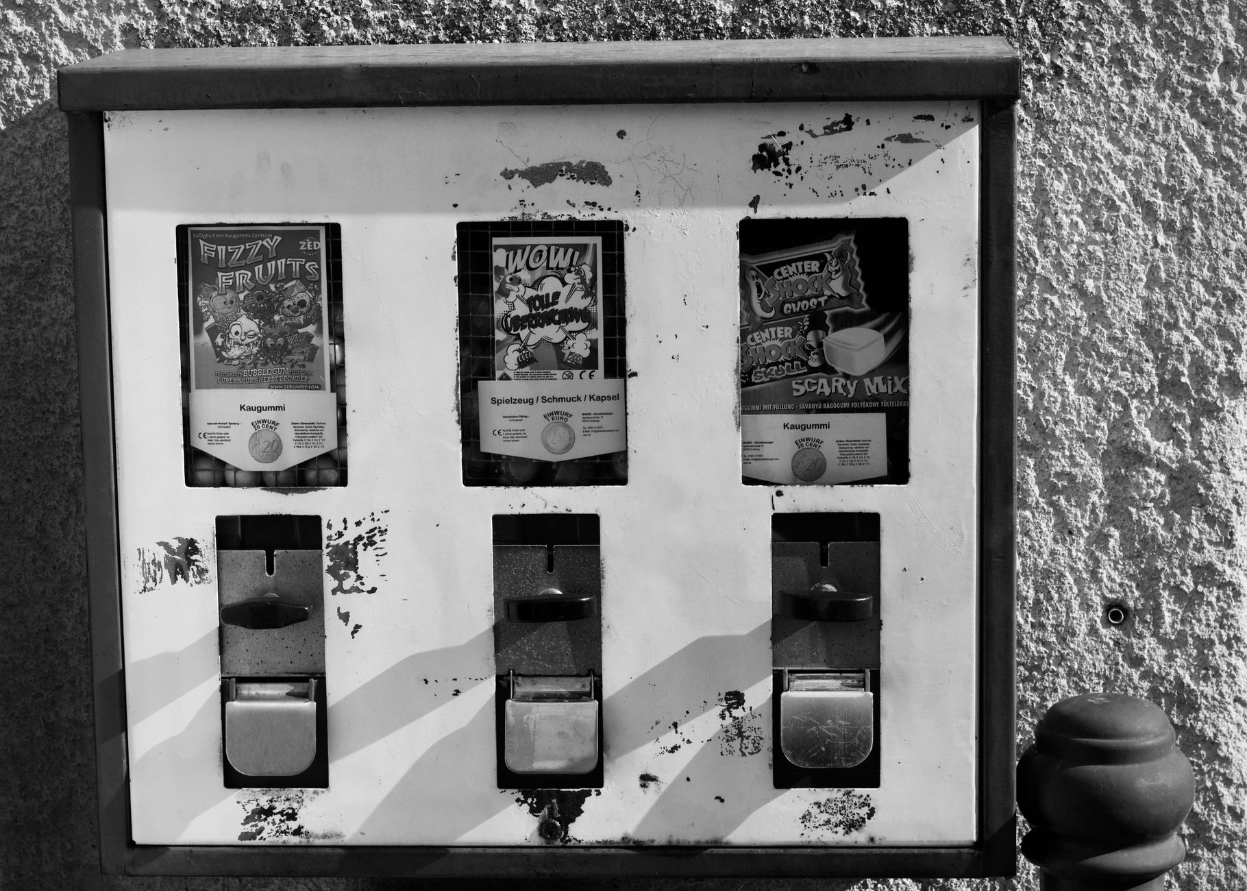 Black and white photo of a retro candy vending machine on a worn wall.