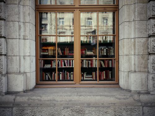 Free A rustic window displaying a collection of books, reflecting city architecture. Stock Photo