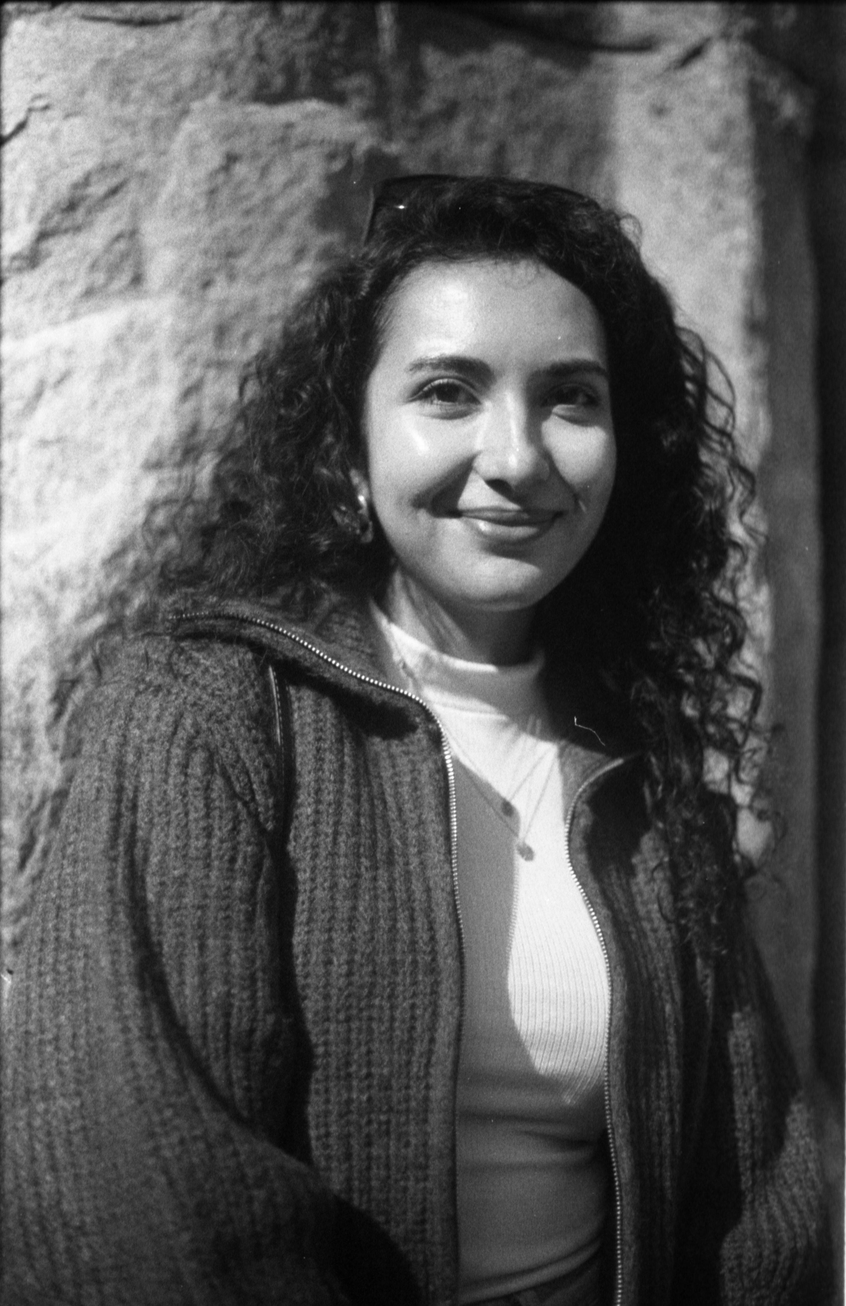 Black and white image of a smiling woman in a sweater outdoors.