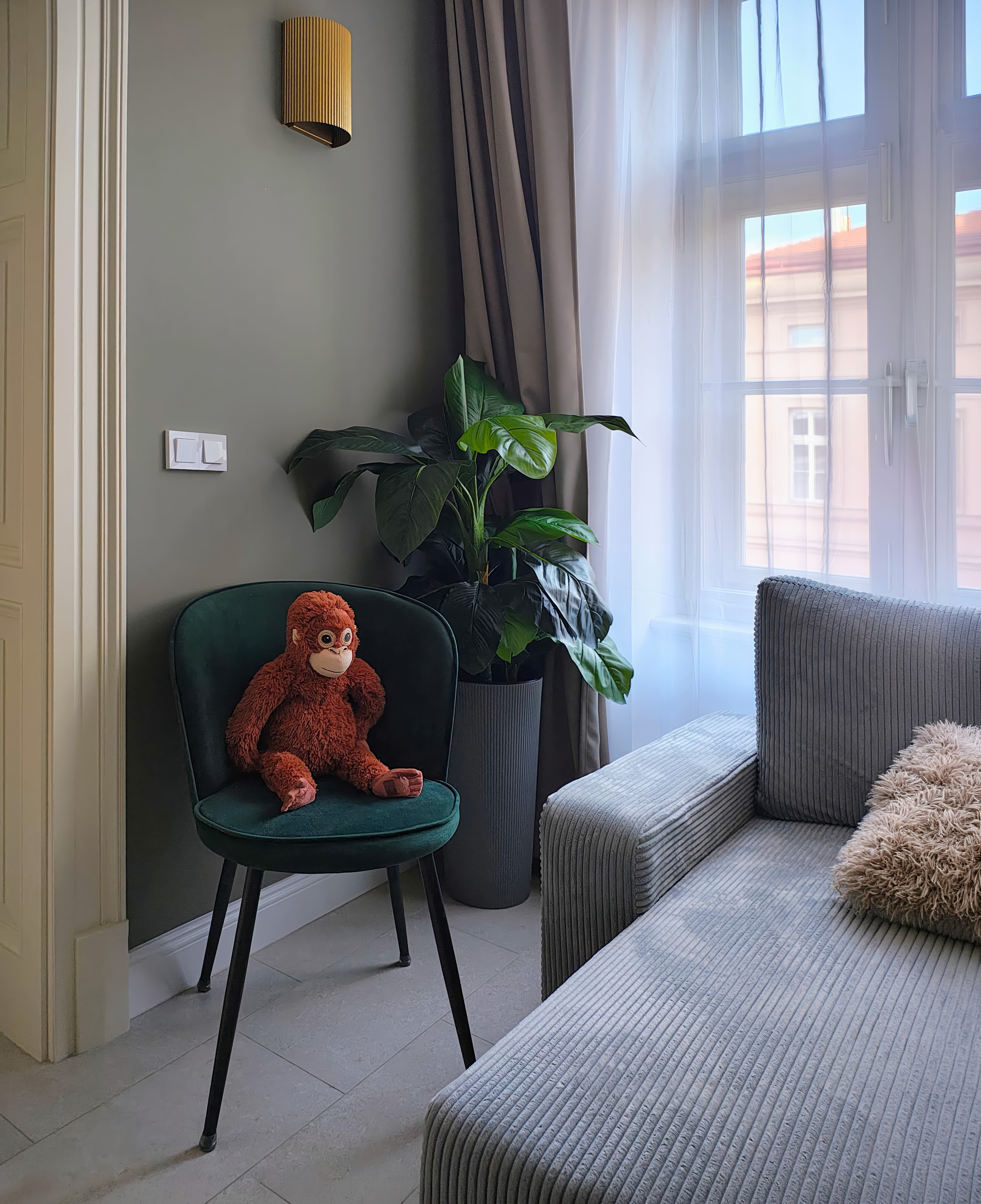 A cozy living room corner with a plush monkey toy, green chair, indoor plant, and modern decor.