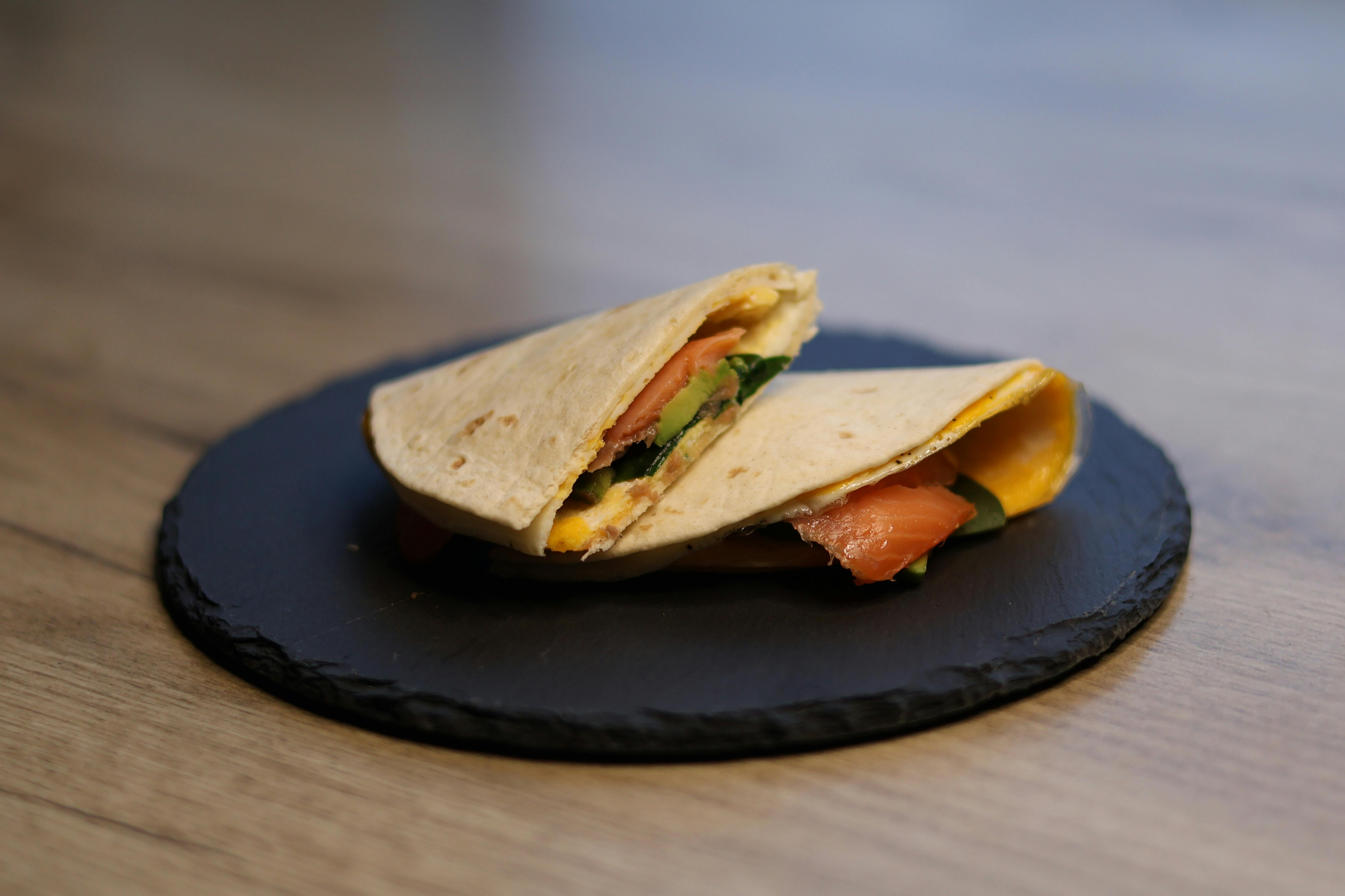A fresh salmon tortilla wrap with spinach and cheese on a slate platter, perfect for a healthy meal.