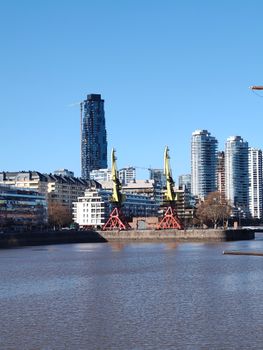 City skyline featuring modern buildings and industrial cranes by the waterfront.
