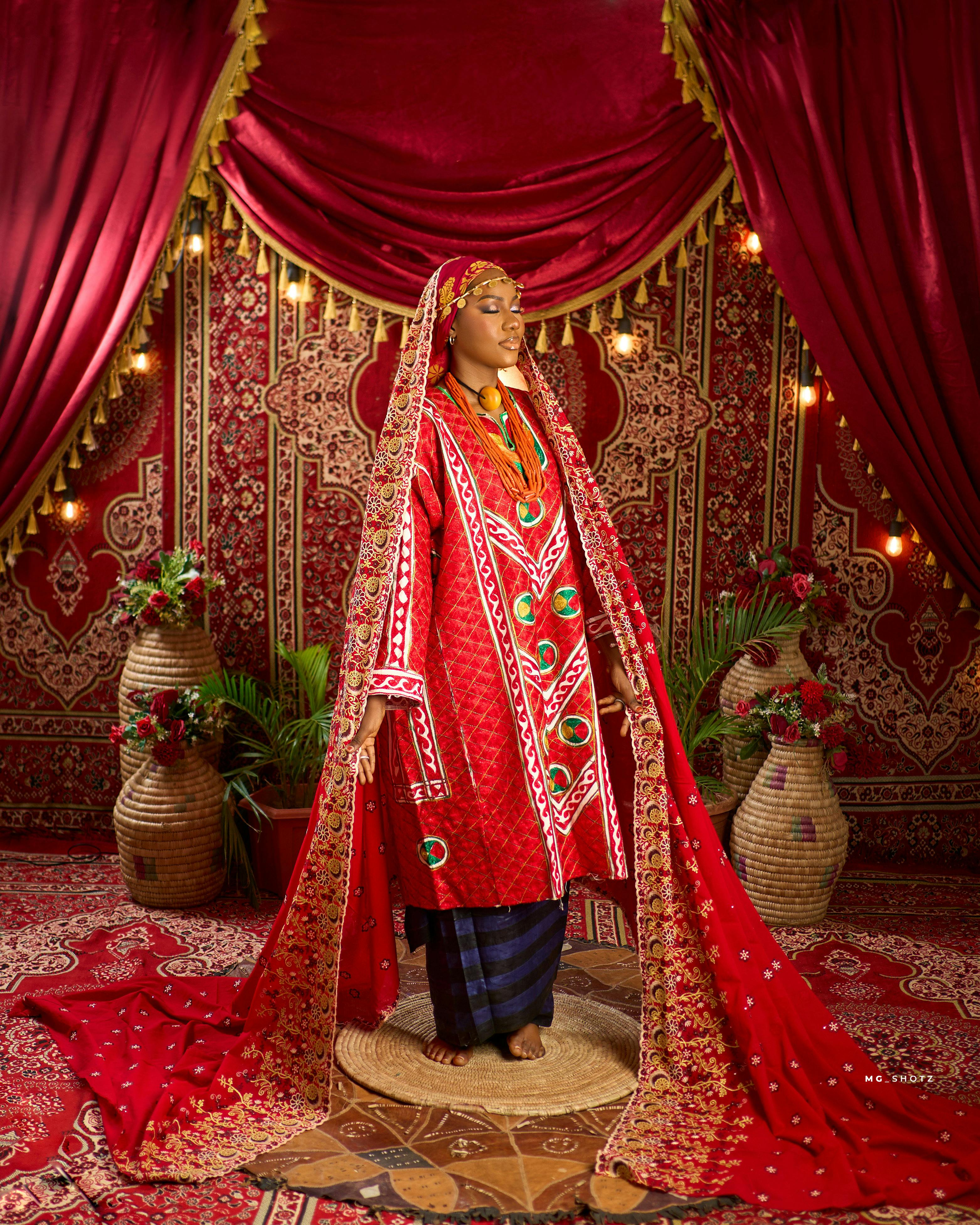 A vibrant portrait of a Nigerian bride in rich traditional attire, captured indoors.