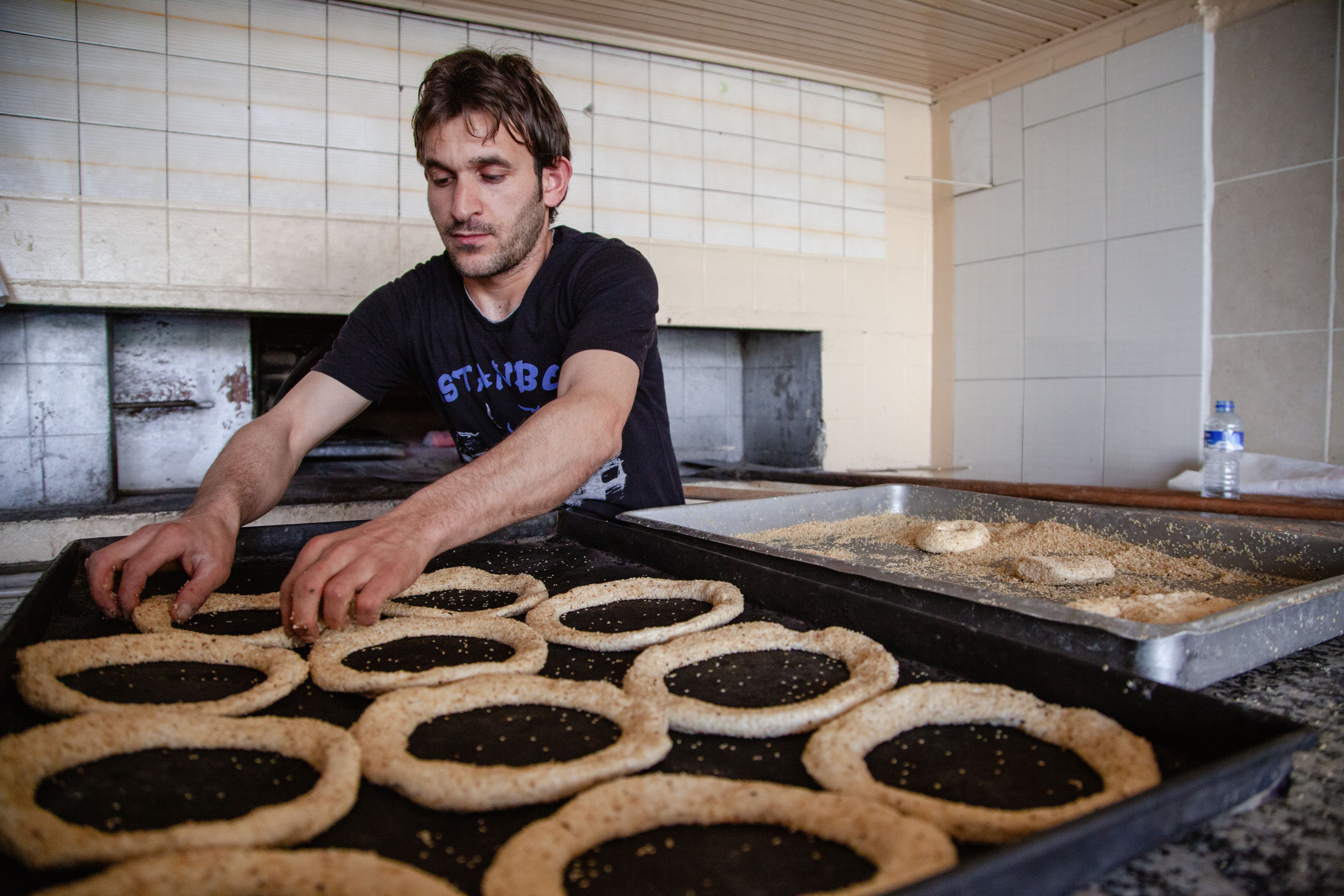 A baker arranges simit on trays in a traditional bakery in Denizli, Türkiye.