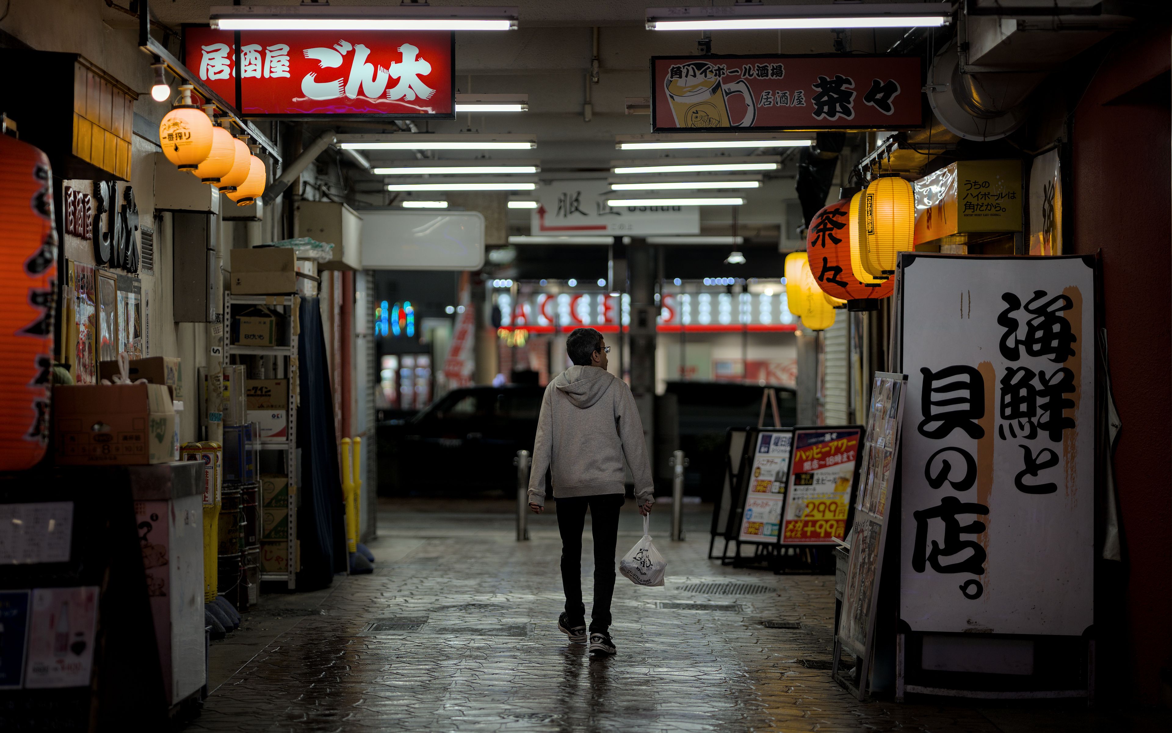 A person walks under glowing lanterns and neon signs in Kobe, Japan at night.
