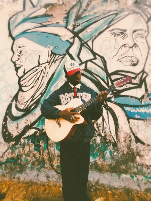 Free A street musician plays guitar in front of a vibrant urban mural, blending art with culture. Stock Photo