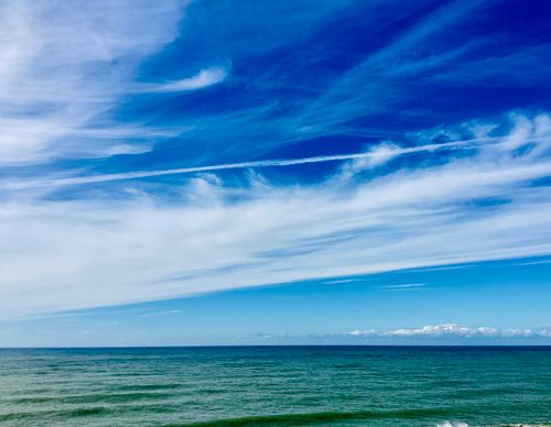 Free Breathtaking view of a calm ocean under a bright blue sky with wispy clouds. Stock Photo