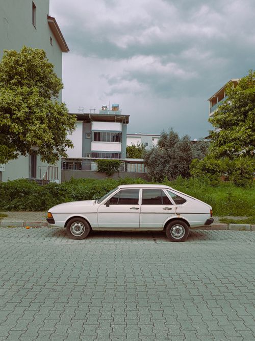 Free Vintage white car parked on a paved street amidst urban greenery and residential buildings. Stock Photo