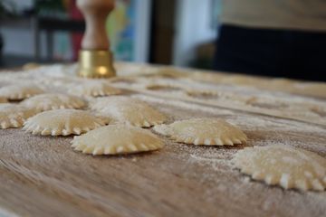 Rows of fluted fresh ravioli on a floured wooden table beside a brass stamp
