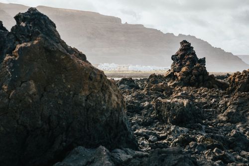 Free Dramatic volcanic rocks in Lanzarote, Canary Islands with distant whitewashed buildings. Stock Photo