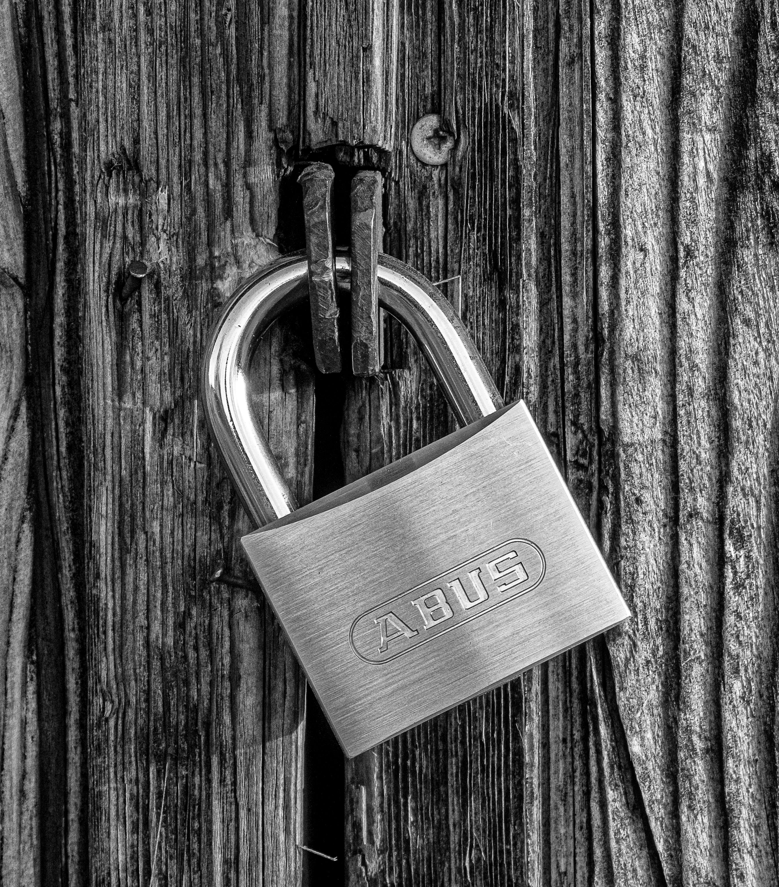 A detailed black and white photo of a metallic padlock securing a wooden door, symbolizing security and protection.